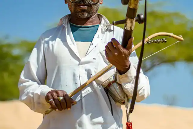 Rajasthani musician in a red turban playing a ravanahatha in the desert